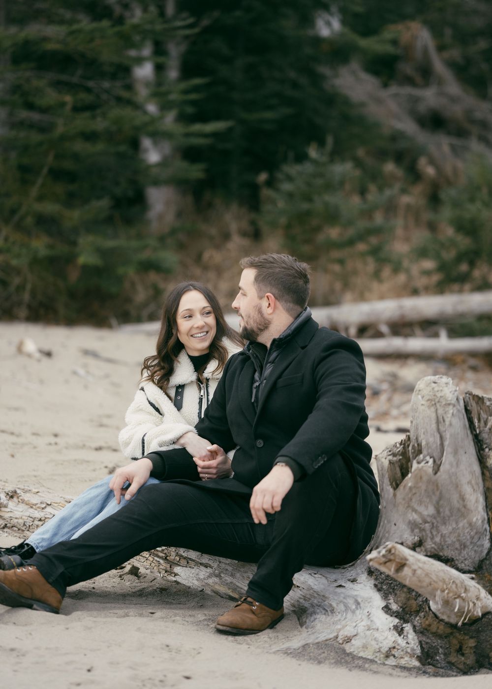 Couple sitting together on driftwood logs at a scenic beach.