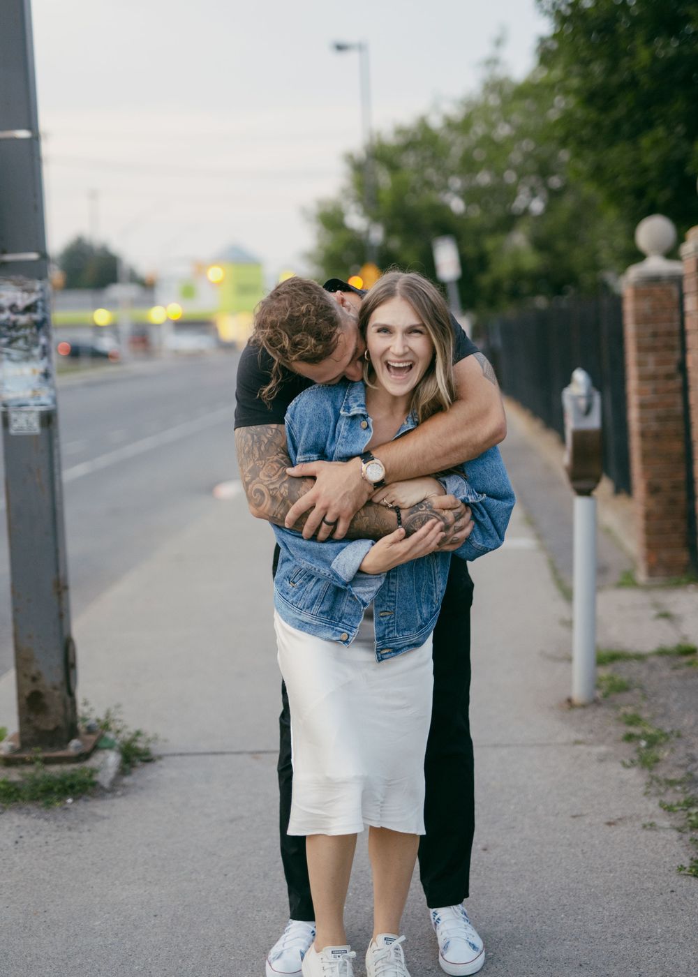 Joyful couple laughing and embracing on urban sidewalk.