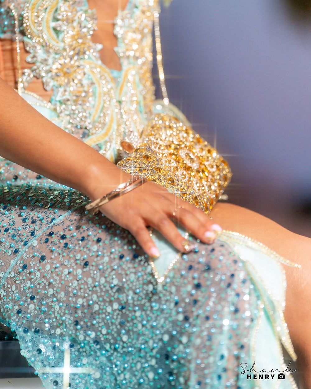 Close-up of a sparkly turquoise formal dress with gold sequin details and a hand resting on the fabric.