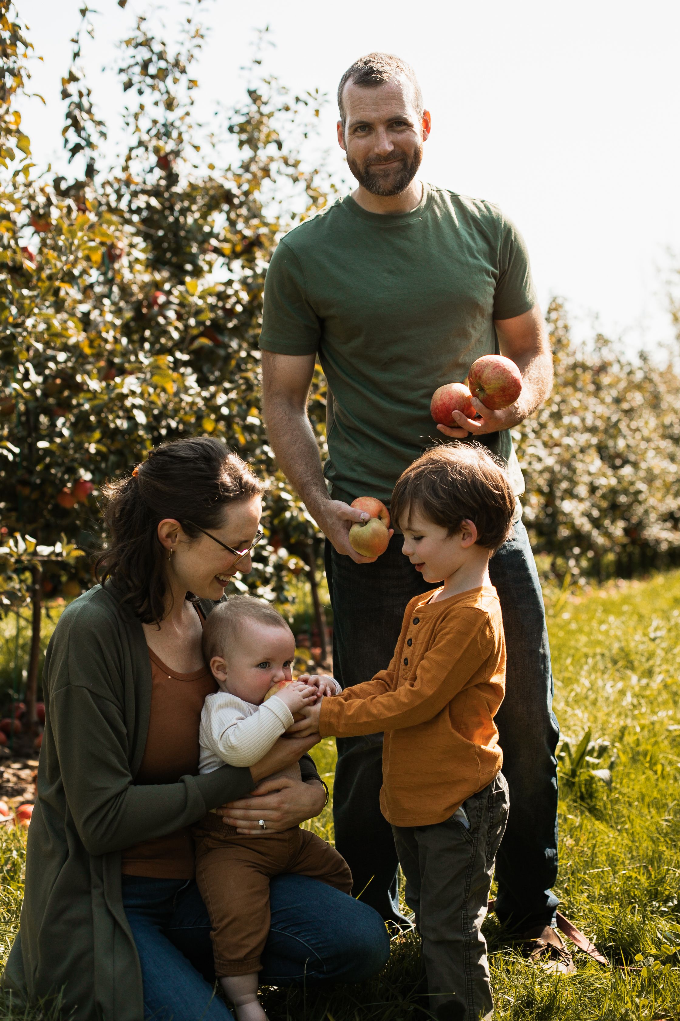 Happy family spending time together outdoors at an apple orchard on a sunny autumn day.