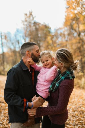 Family shares a tender moment outdoors during autumn with fallen leaves and warm golden light in background.