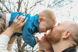 A tender moment shared between a baby in blue and an adult outdoors against a backdrop of bare tree branches.