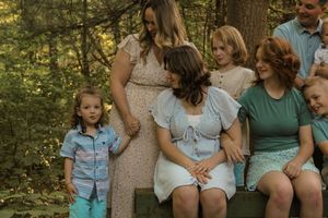 A family group sits together outdoors in a wooded setting during a casual summer photo session.