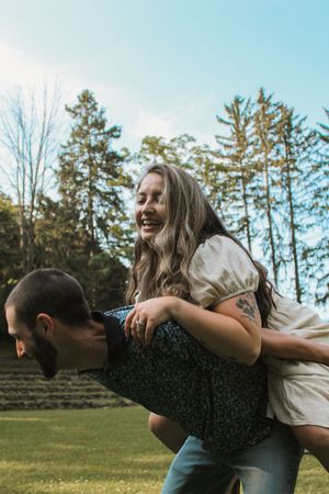 Two people enjoying a playful moment outdoors with pine trees and blue sky in the background.