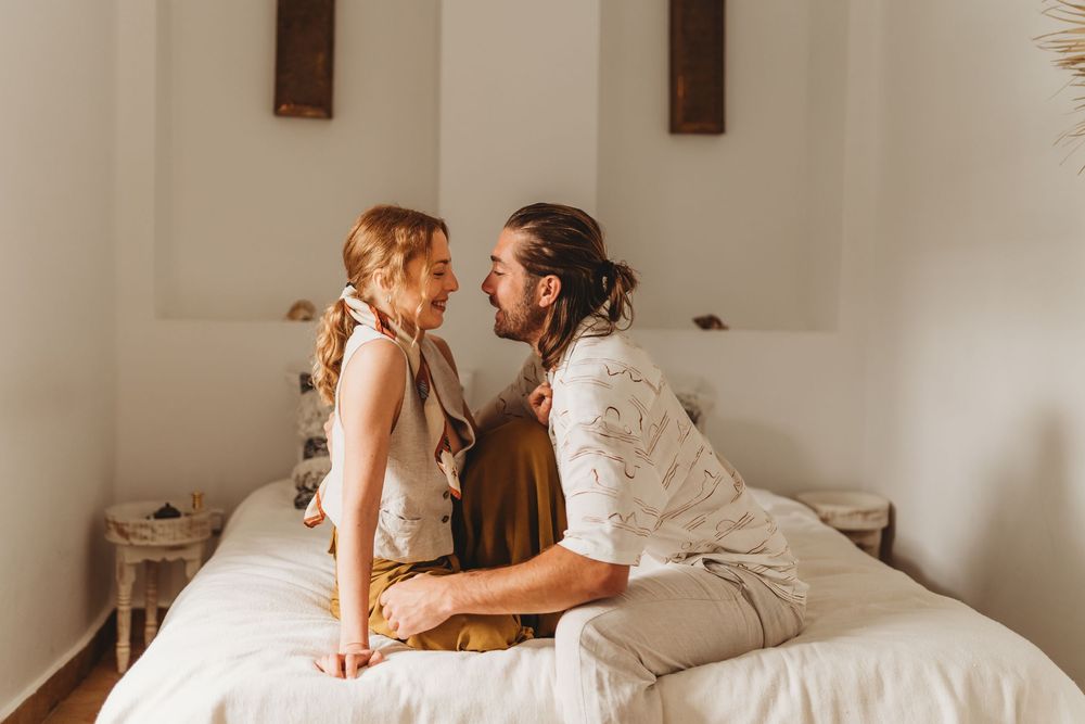 A touching intimate moment between two people on a bright white bed in a minimalist bedroom.