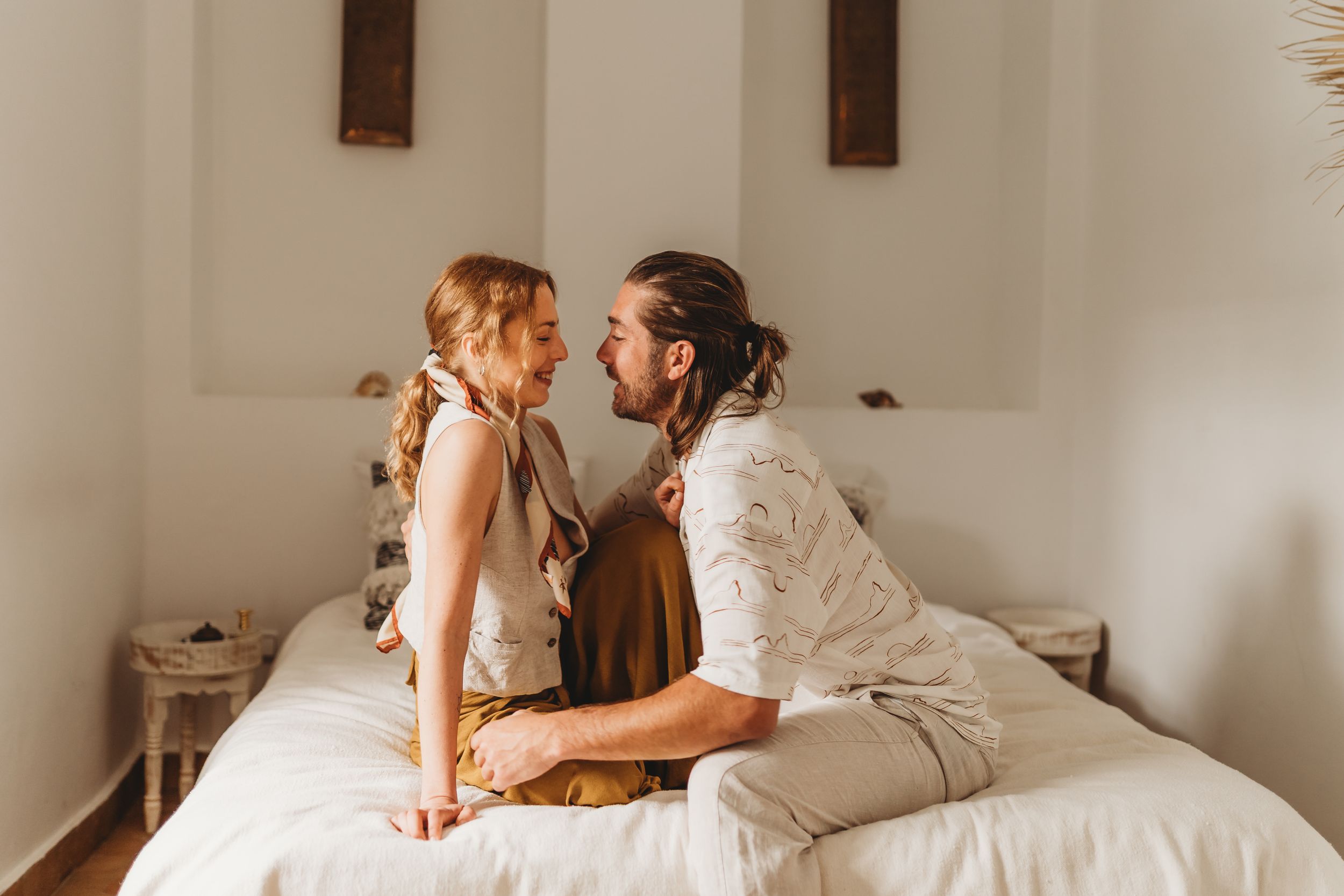 A touching intimate moment between two people on a bright white bed in a minimalist bedroom.