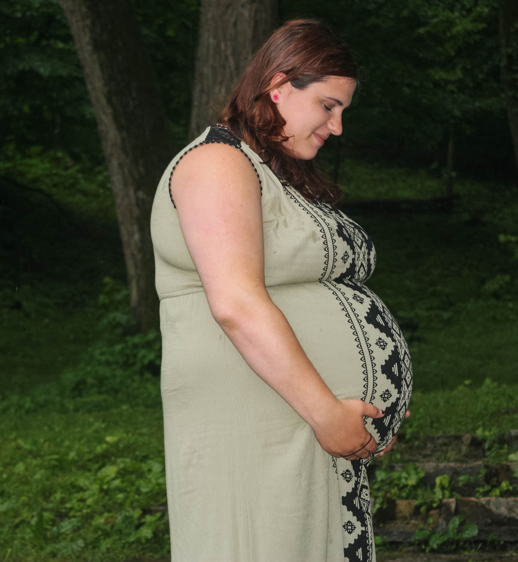 A person wearing a sage green embroidered top poses for maternity photos outdoors.