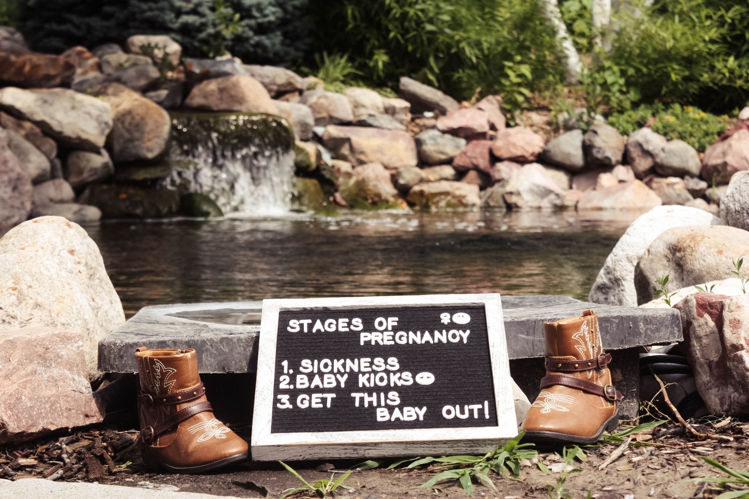 A collection of brown leather shoes arranged on rocky terrain near water.