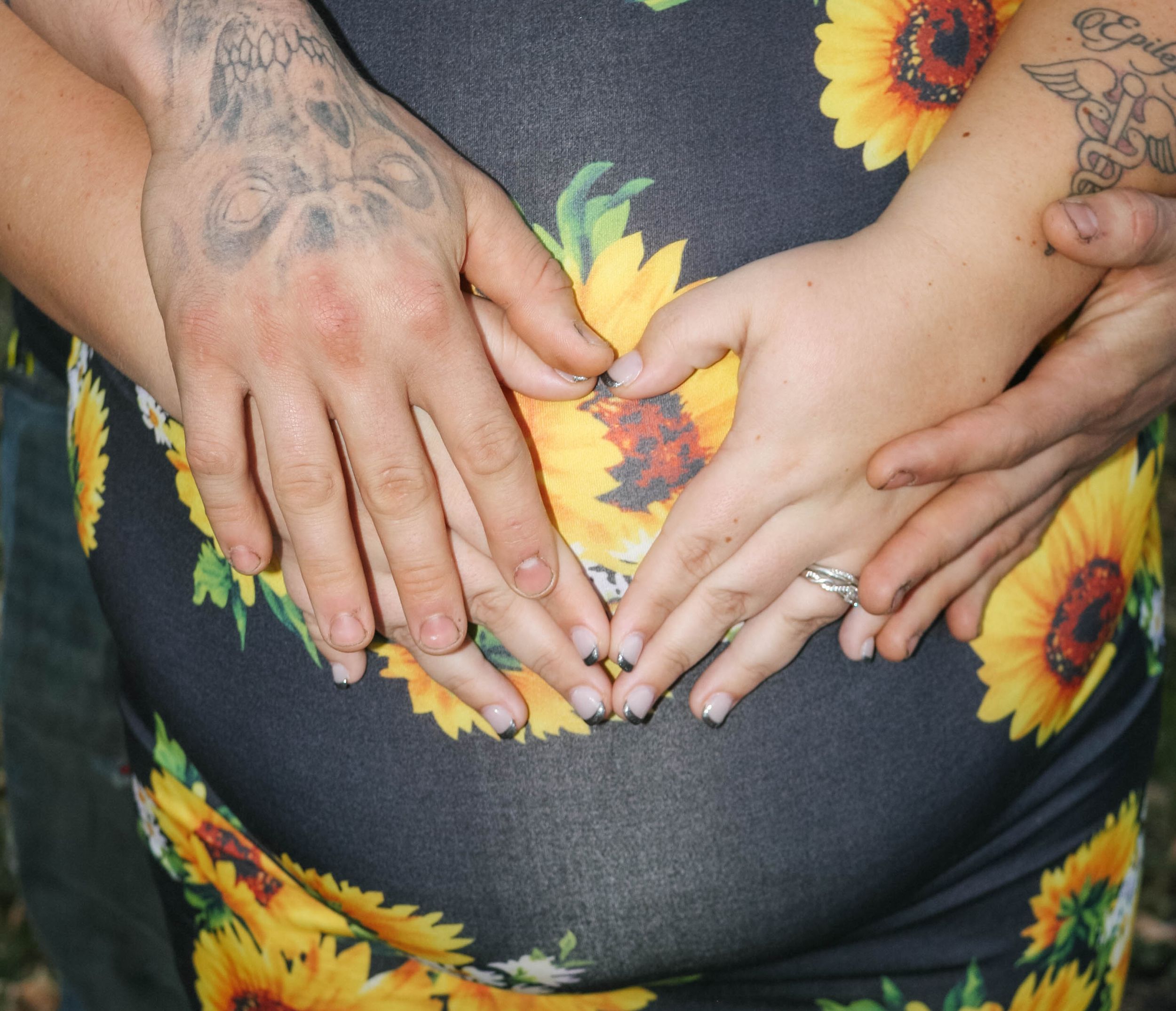 Hands rest on a pregnant belly with sunflower pattern fabric.