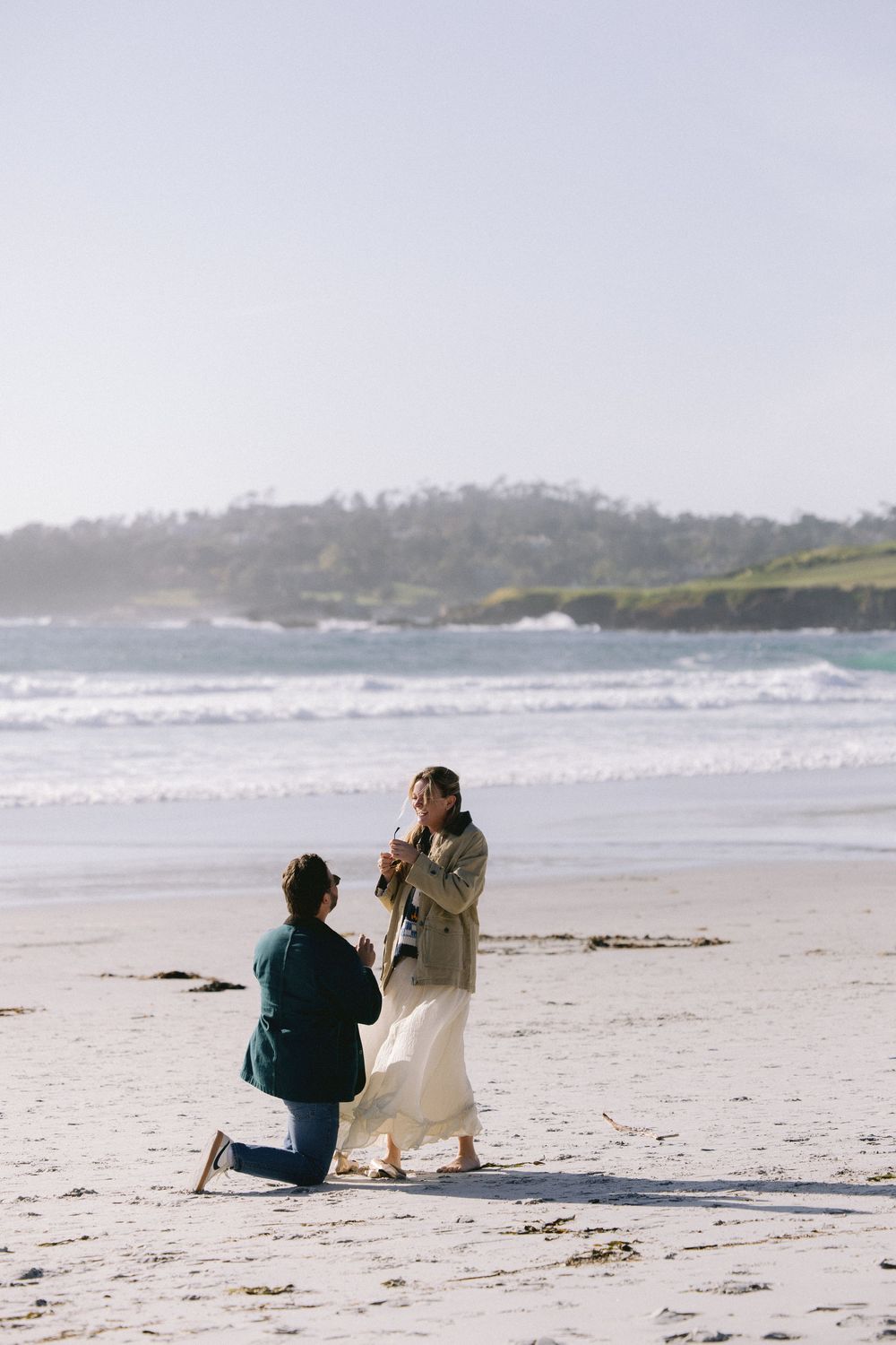 A couple shares a special moment during a proposal on a misty beach with waves crashing in the background.