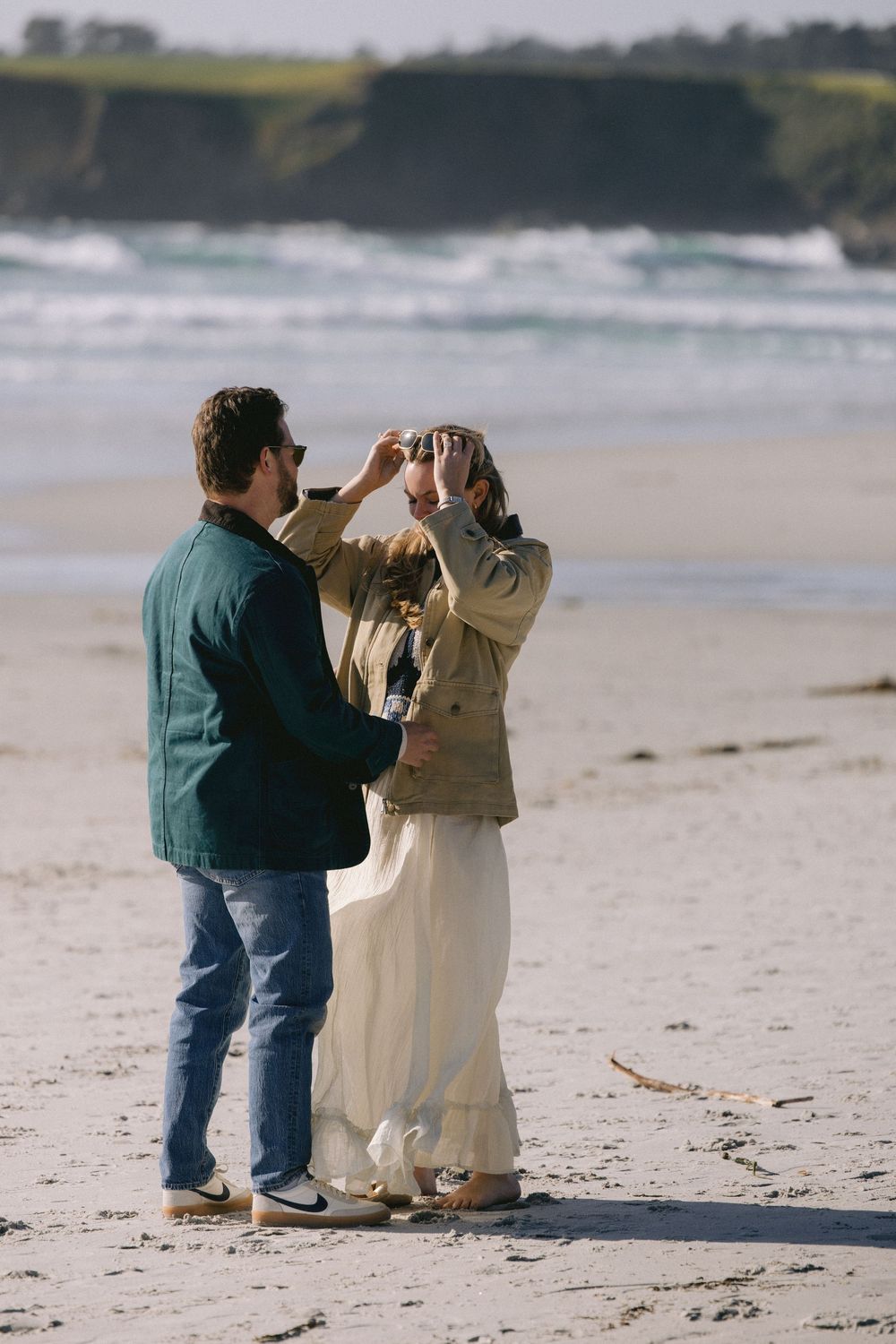 A couple shares a celebratory moment together on a scenic beach with crashing waves and coastal cliffs.