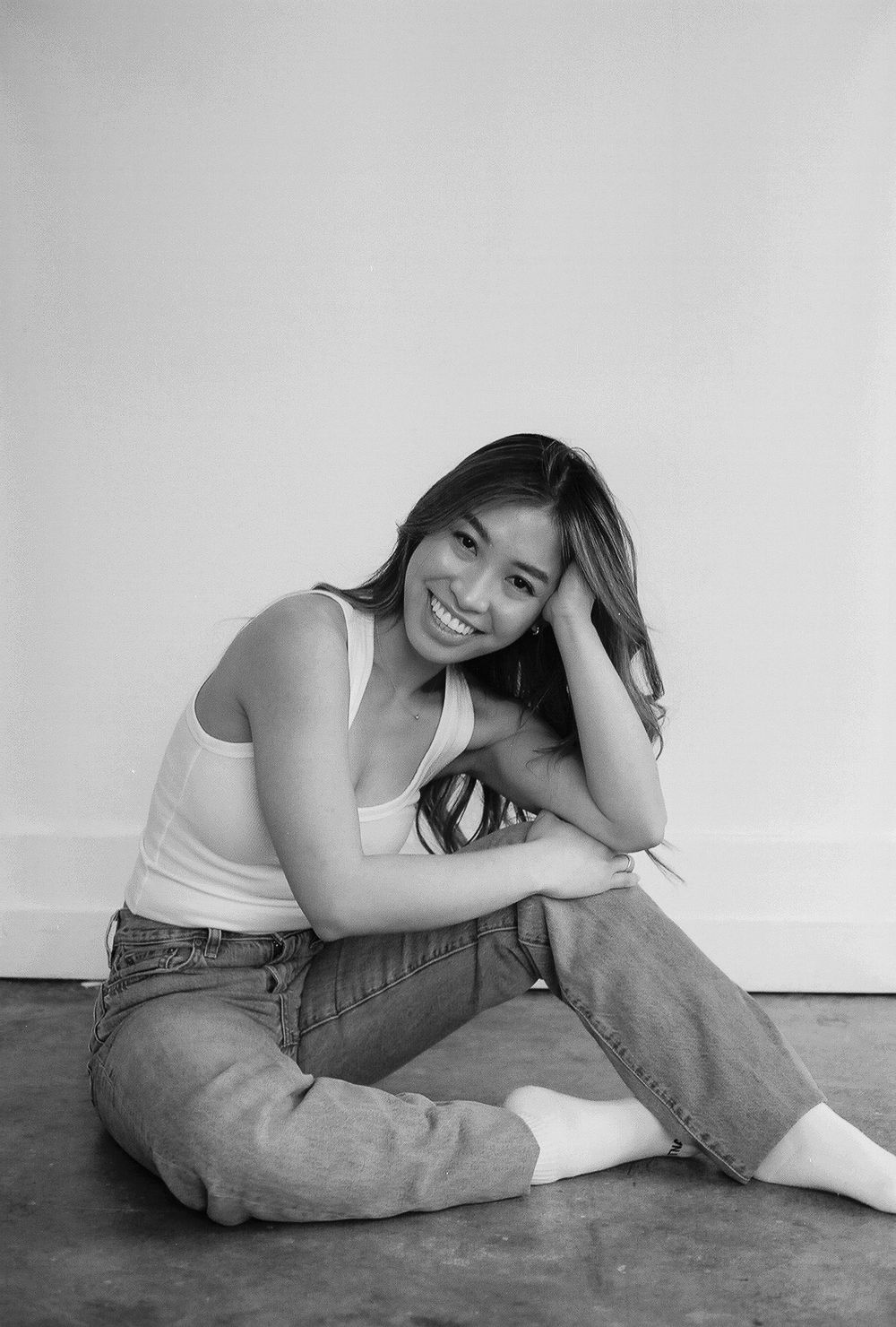 Relaxed lifestyle poses wearing casual white tank top and jeans on floor.