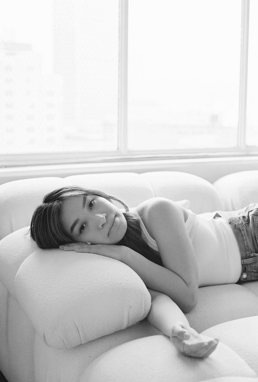 Contemplative black and white portraits lying on white pillows near window.