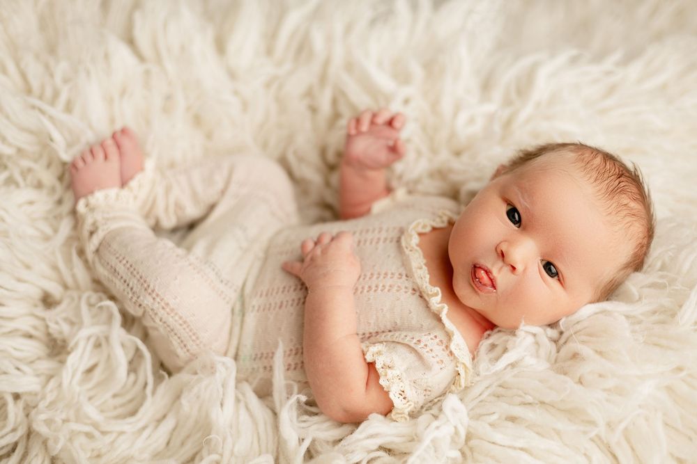 A newborn baby lying on soft white fur wearing knitted clothing.