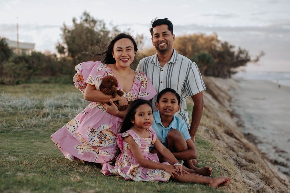 Happy family laughing together while sitting on grassy cliff at sunset by the beach.