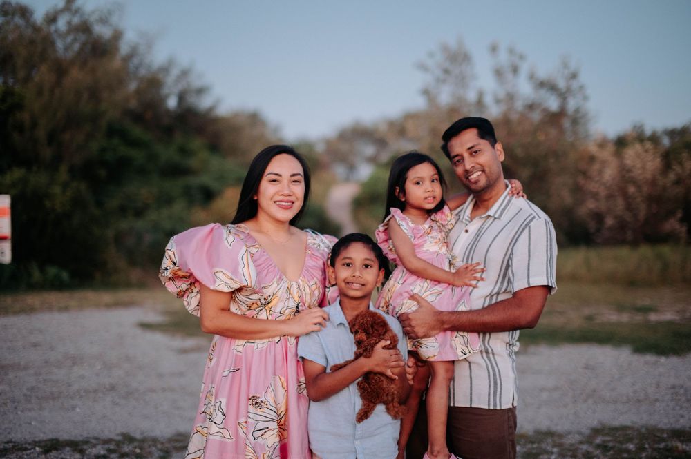 A family of four stands together outdoors at sunset against a natural backdrop with trees.