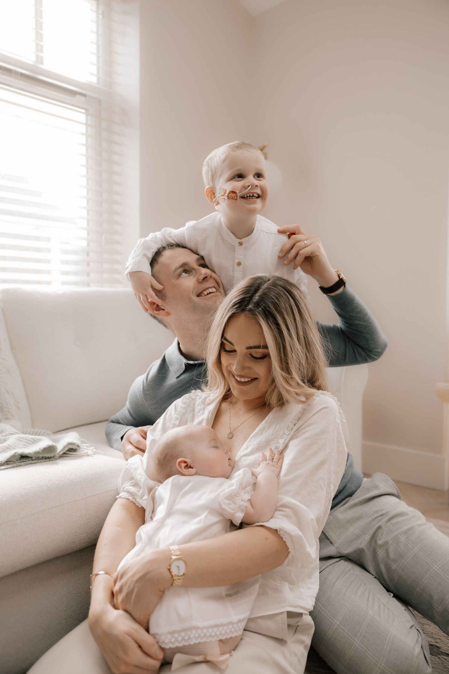 Intimate family moment at home shows parents and children cuddling together on a cozy white couch by the window.