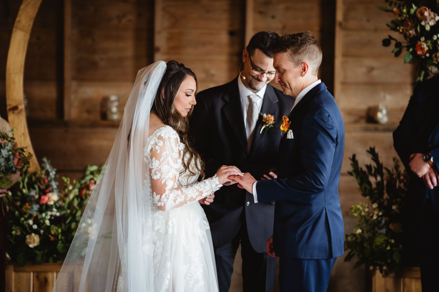 A beautiful wedding ceremony shows a couple exchanging rings with the officiant in a rustic wooden venue.