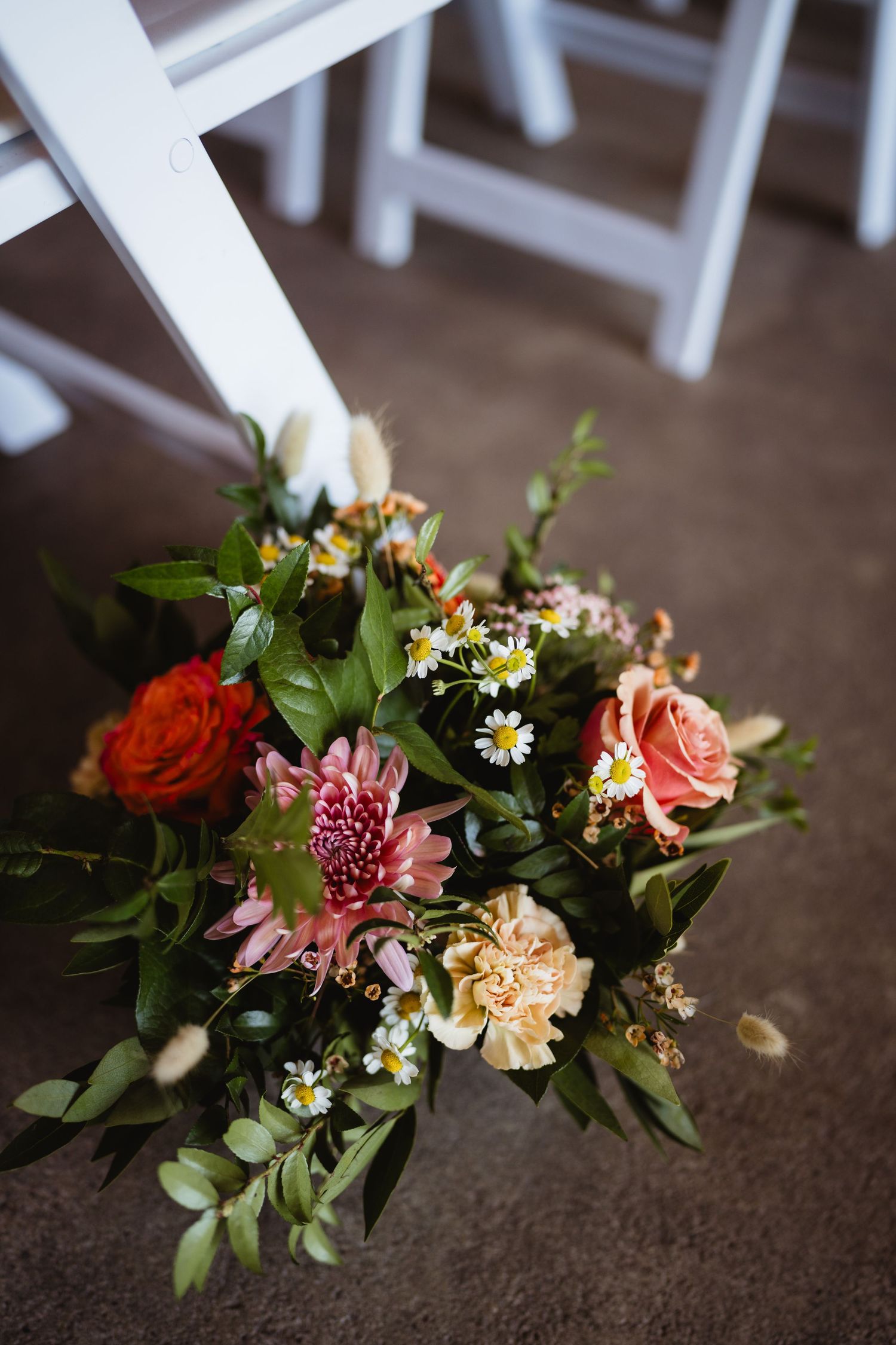 A vibrant floral arrangement featuring pink and orange roses, carnations, and daisies with green foliage on a wooden floor.