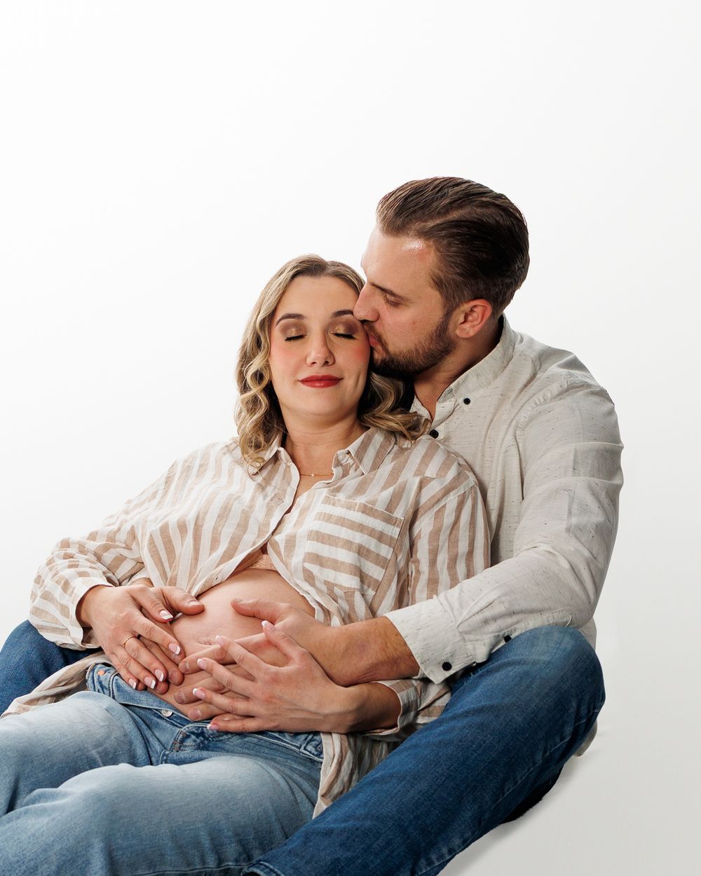 A couple in white and denim share intimate moments while sitting together against a light background.