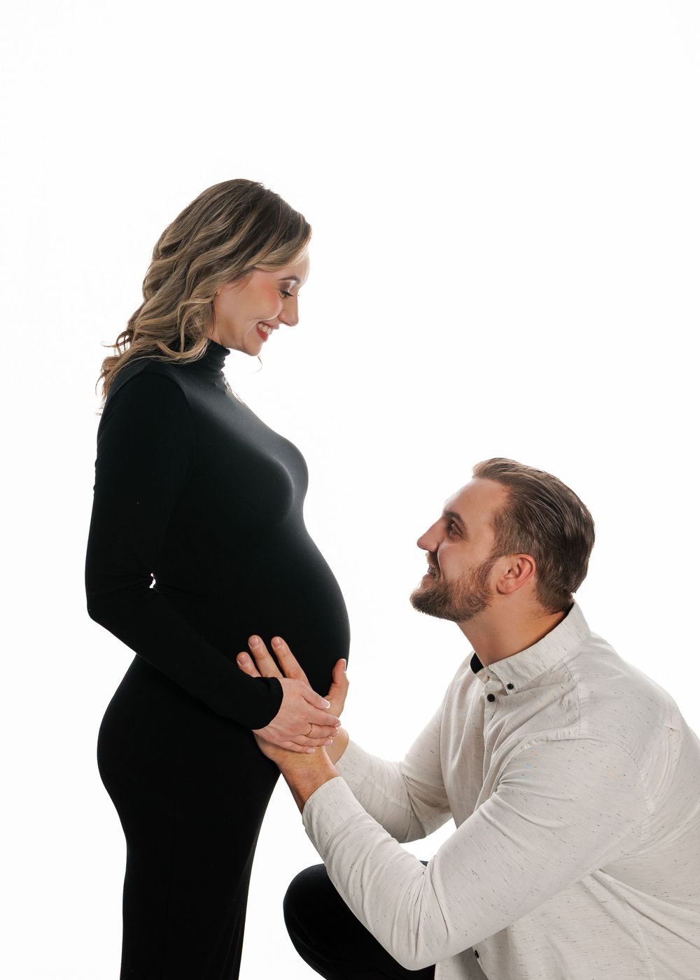 A couple shares an intimate maternity portrait against a white background as they anticipate their new arrival.
