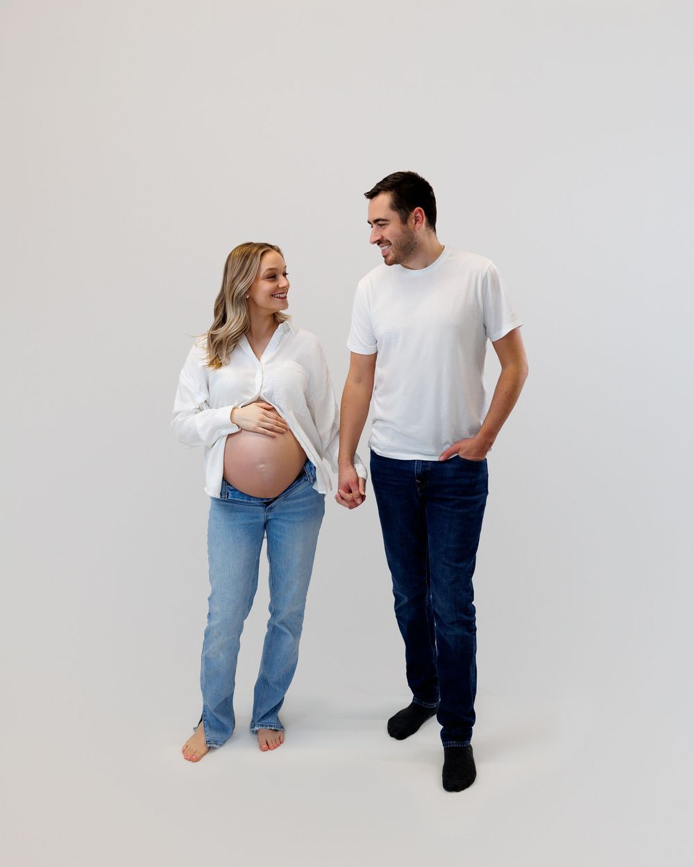 A couple in white shirts and jeans share tender moments in a maternity photo sequence against a light background.