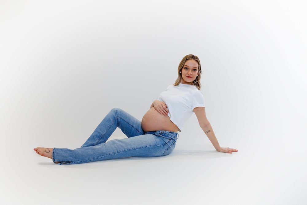 Woman in light blue jeans and white top lounging on white background in casual pose.