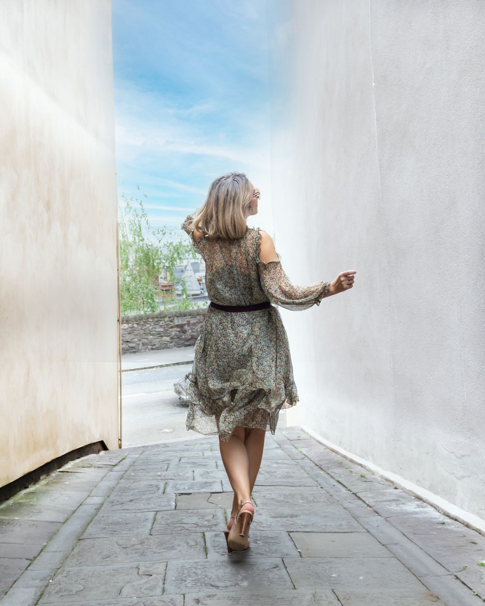 A whimsical back view of someone walking in a floral dress down a white corridor.