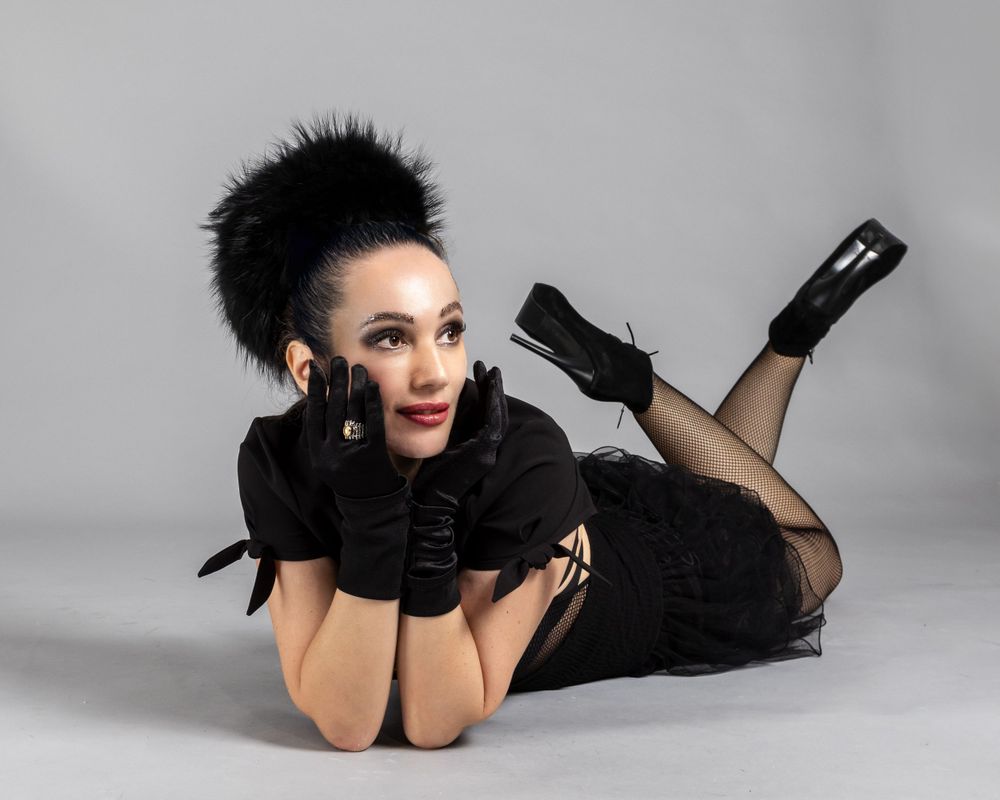 Dramatic fashion photo with black feathers, gloves and glamorous styling against gray studio backdrop.