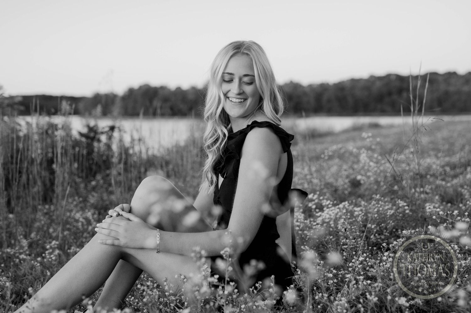 Black and white portrait of person sitting in flowering meadow by lake.