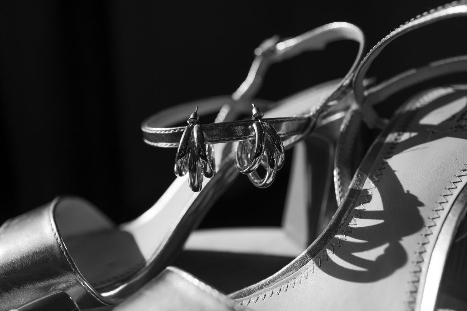 Close-up black and white photo of wedding rings hanging on bridal shoes.