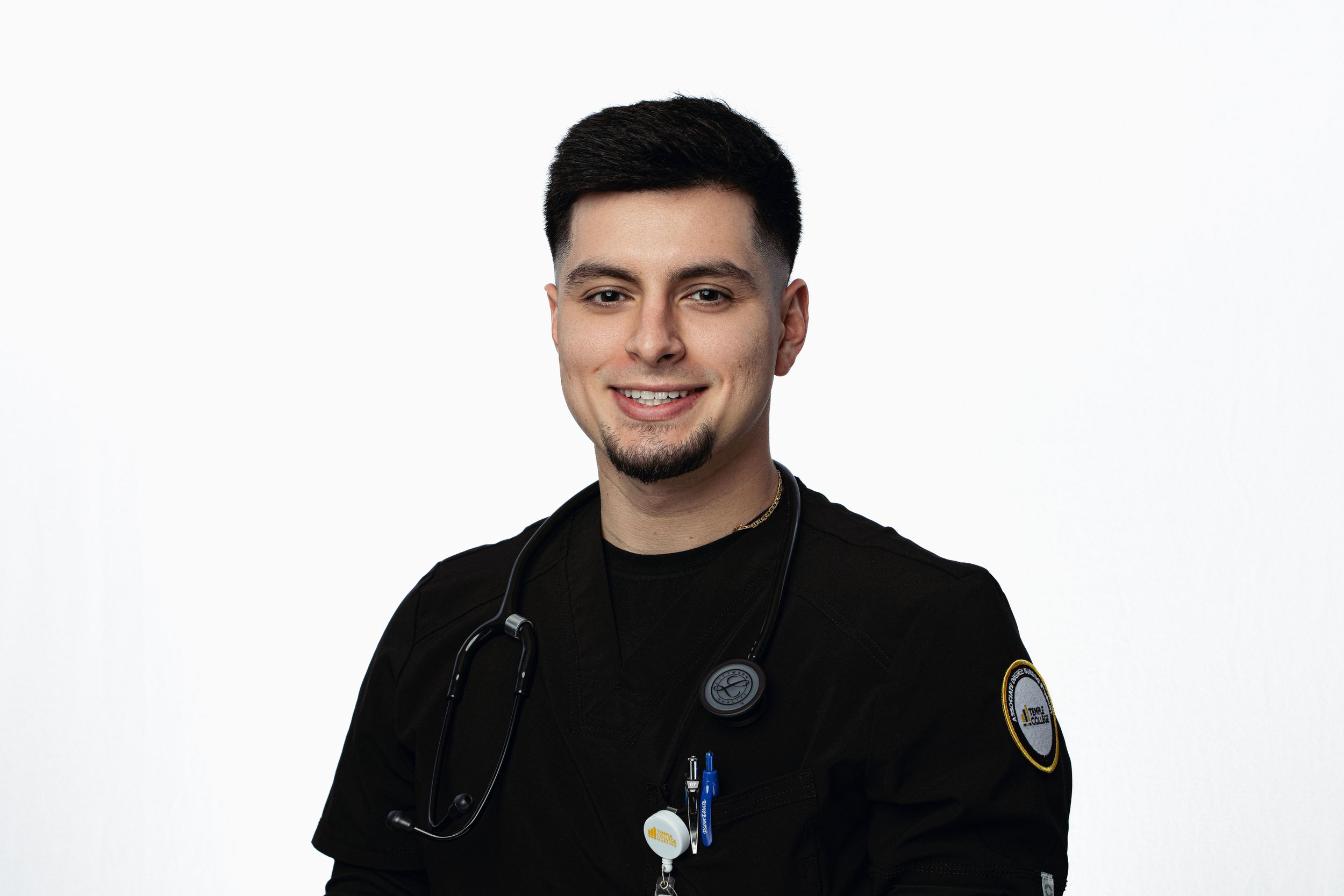 Healthcare worker in black uniform with stethoscope smiling against white background.