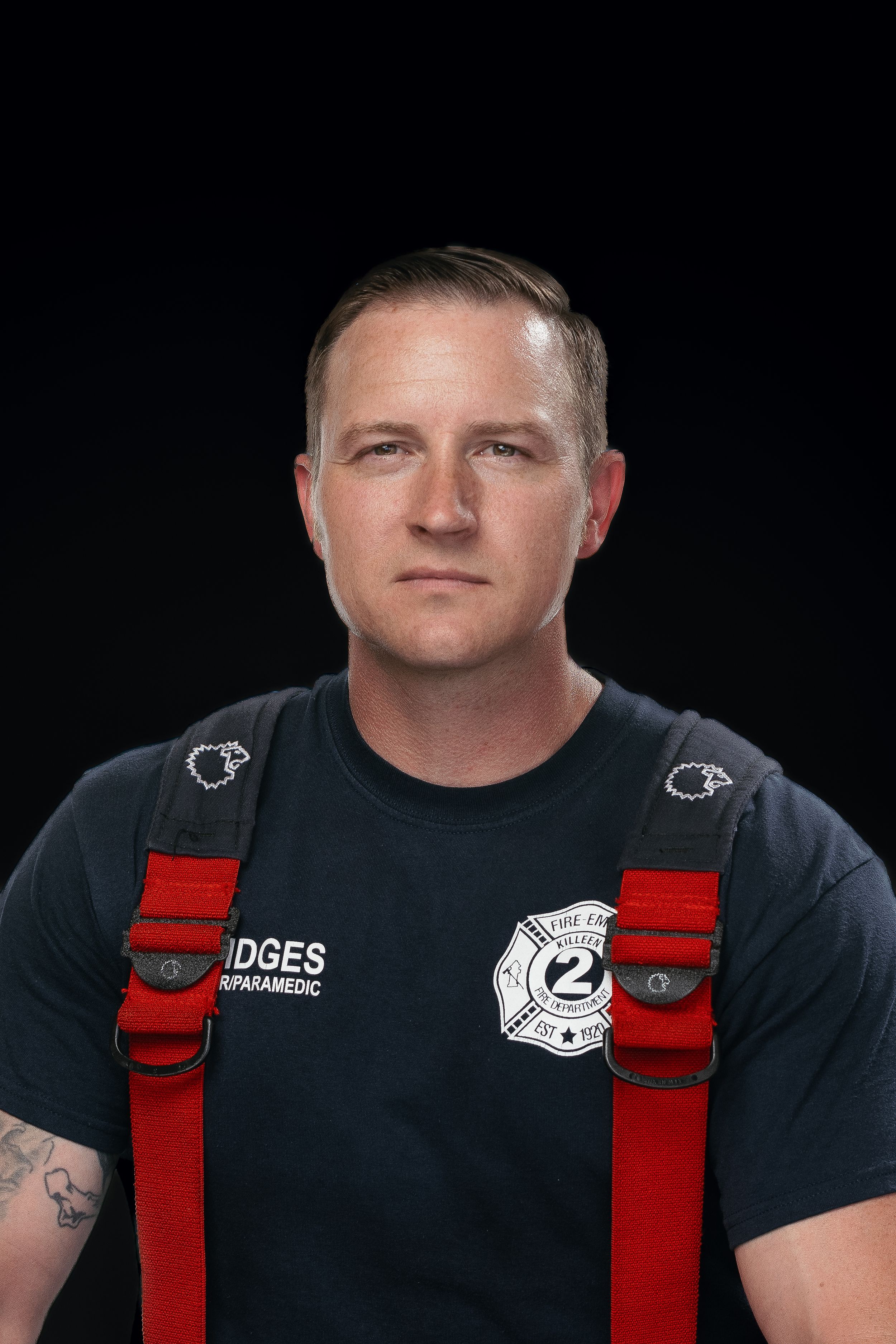 Portrait of someone wearing a black t-shirt with fire department insignia and red suspenders.