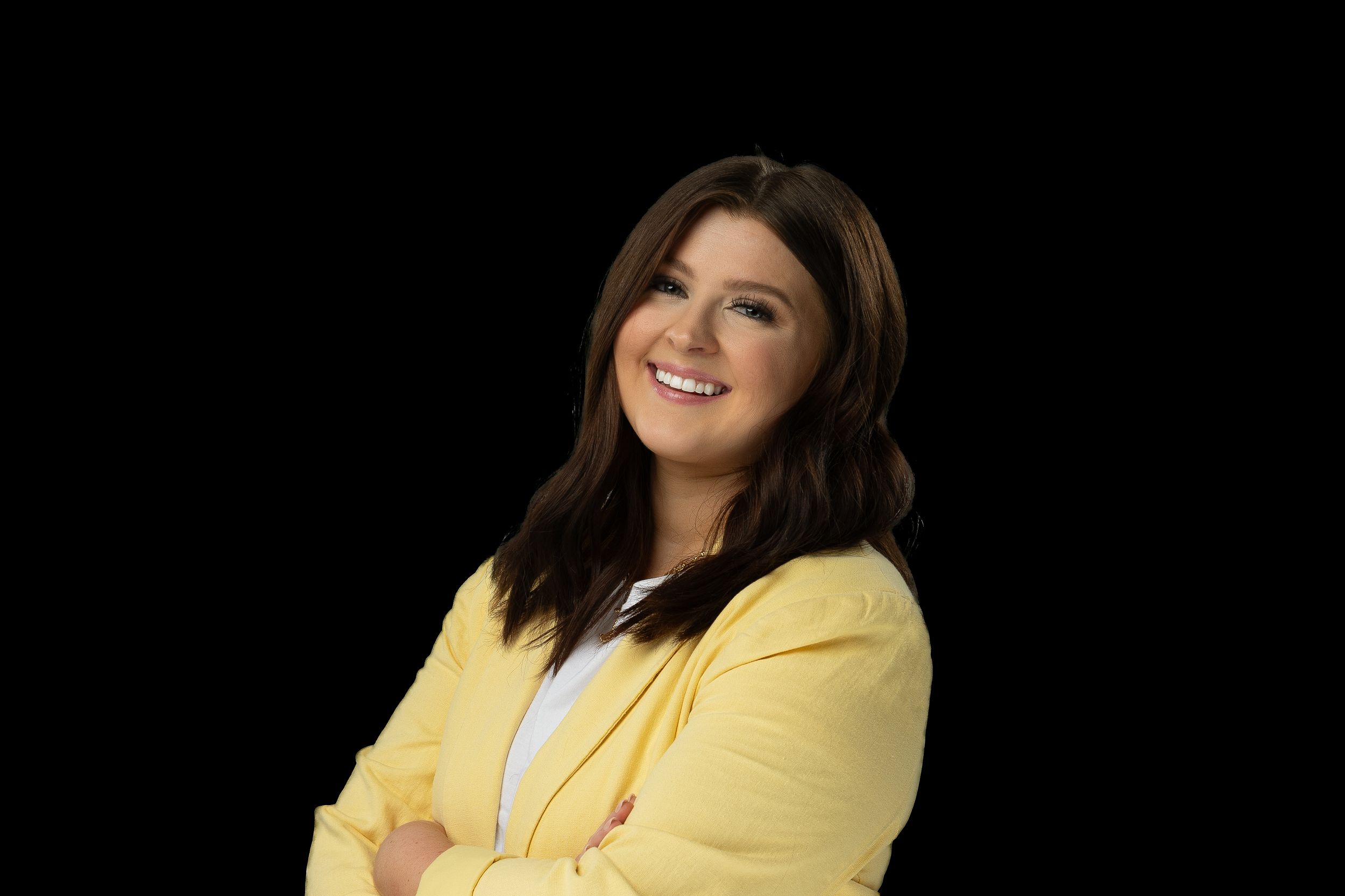 Professional portrait of someone in a yellow blazer smiling against a black background.