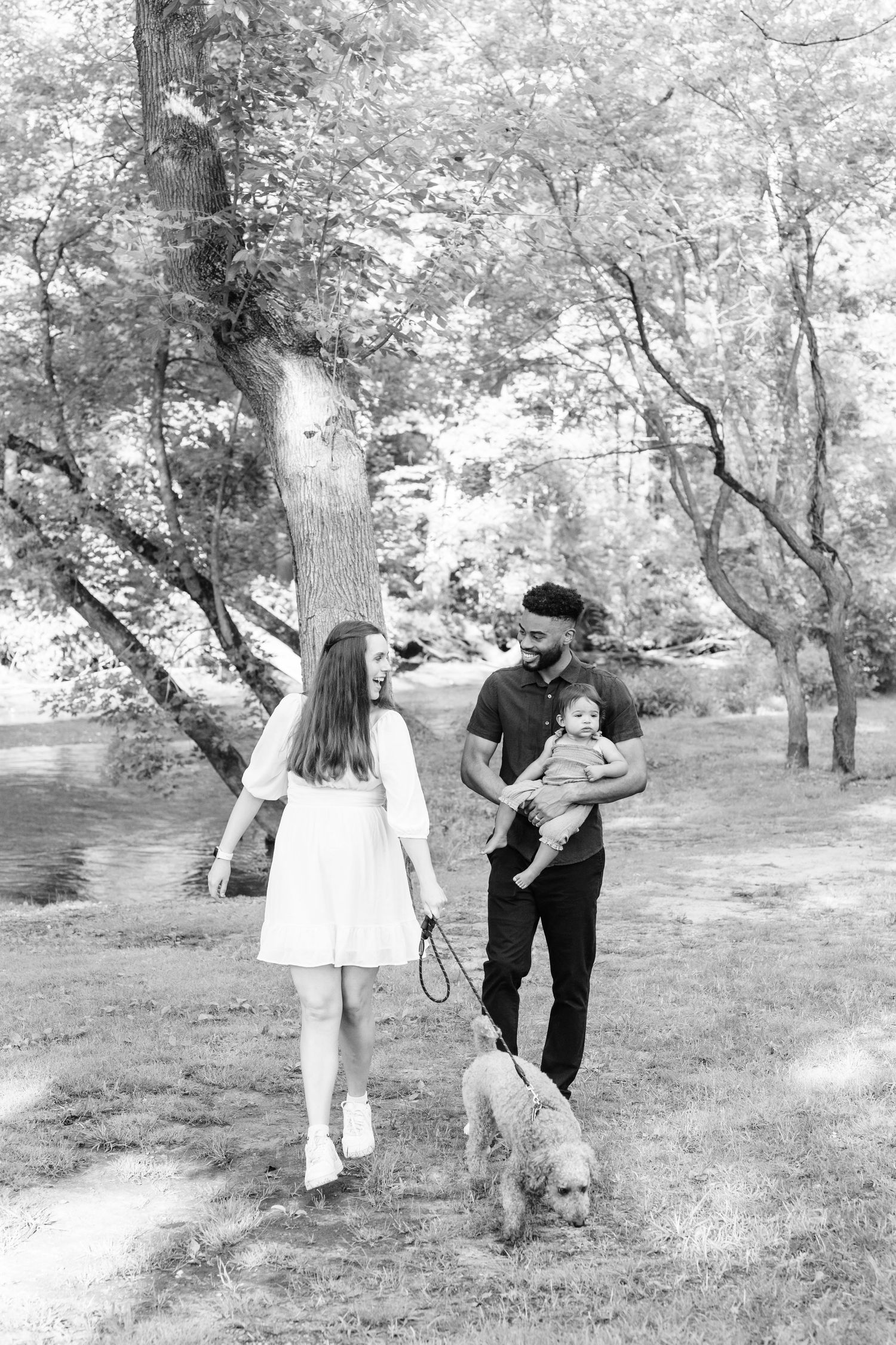 A couple walking their dog in a serene black and white park setting.