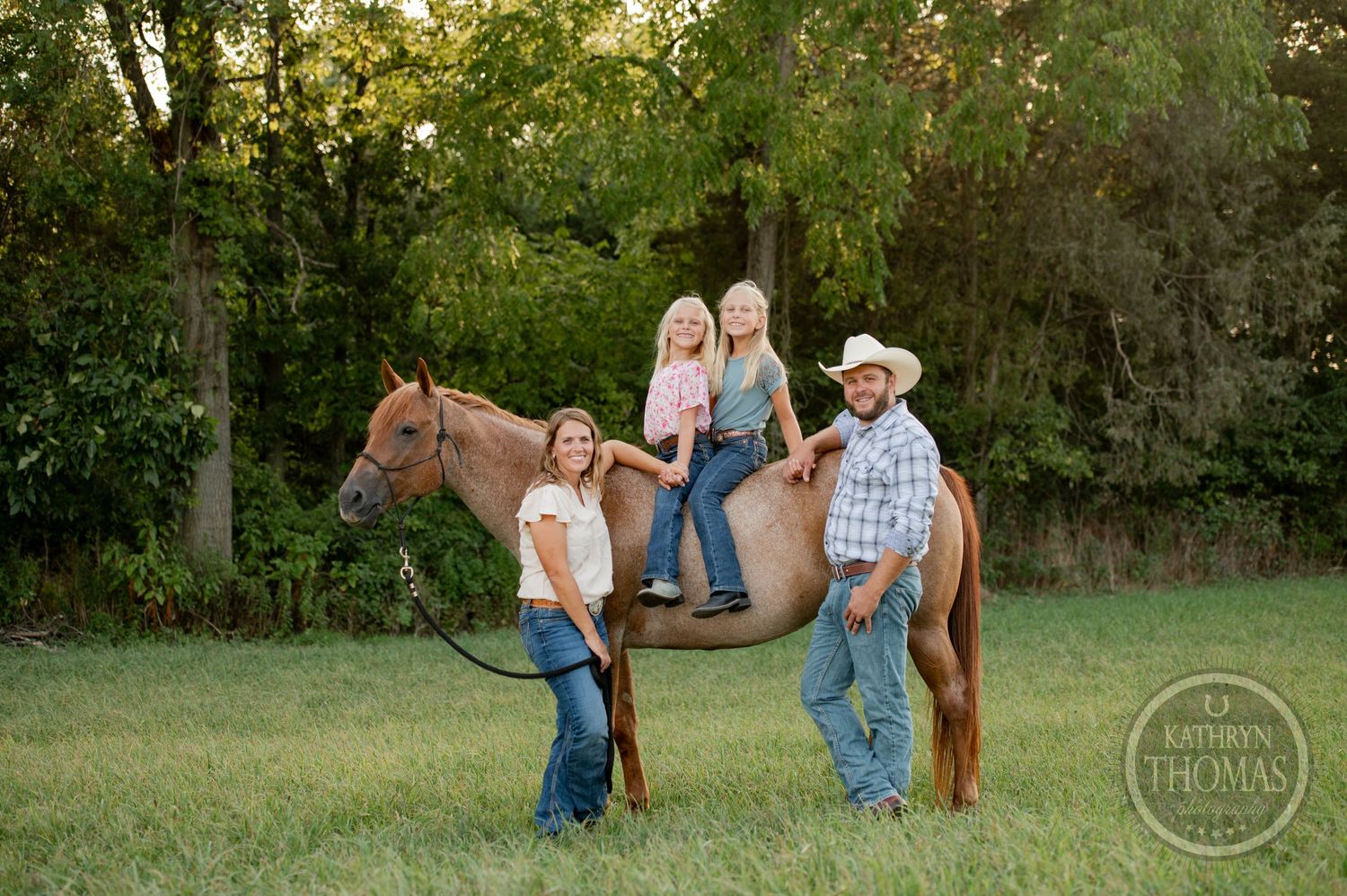 A family poses with their brown horse in a grassy field at sunset.