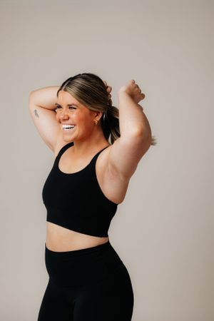 Confident woman in black athletic wear smiling and posing against neutral background in fitness photography session.