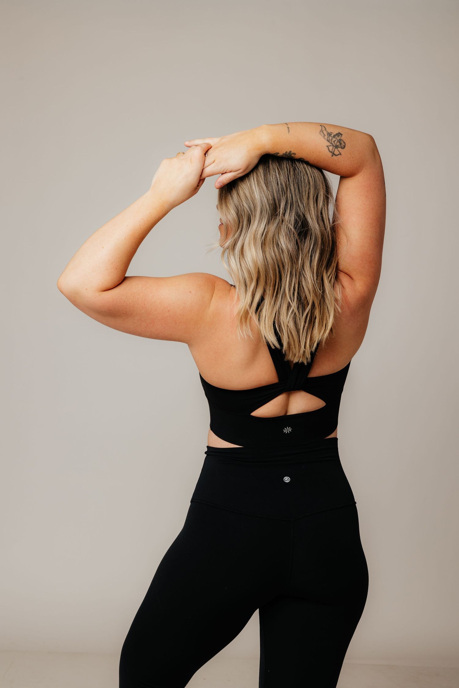 Back view of athletic woman wearing black workout set with cross-back sports bra and high waisted leggings.