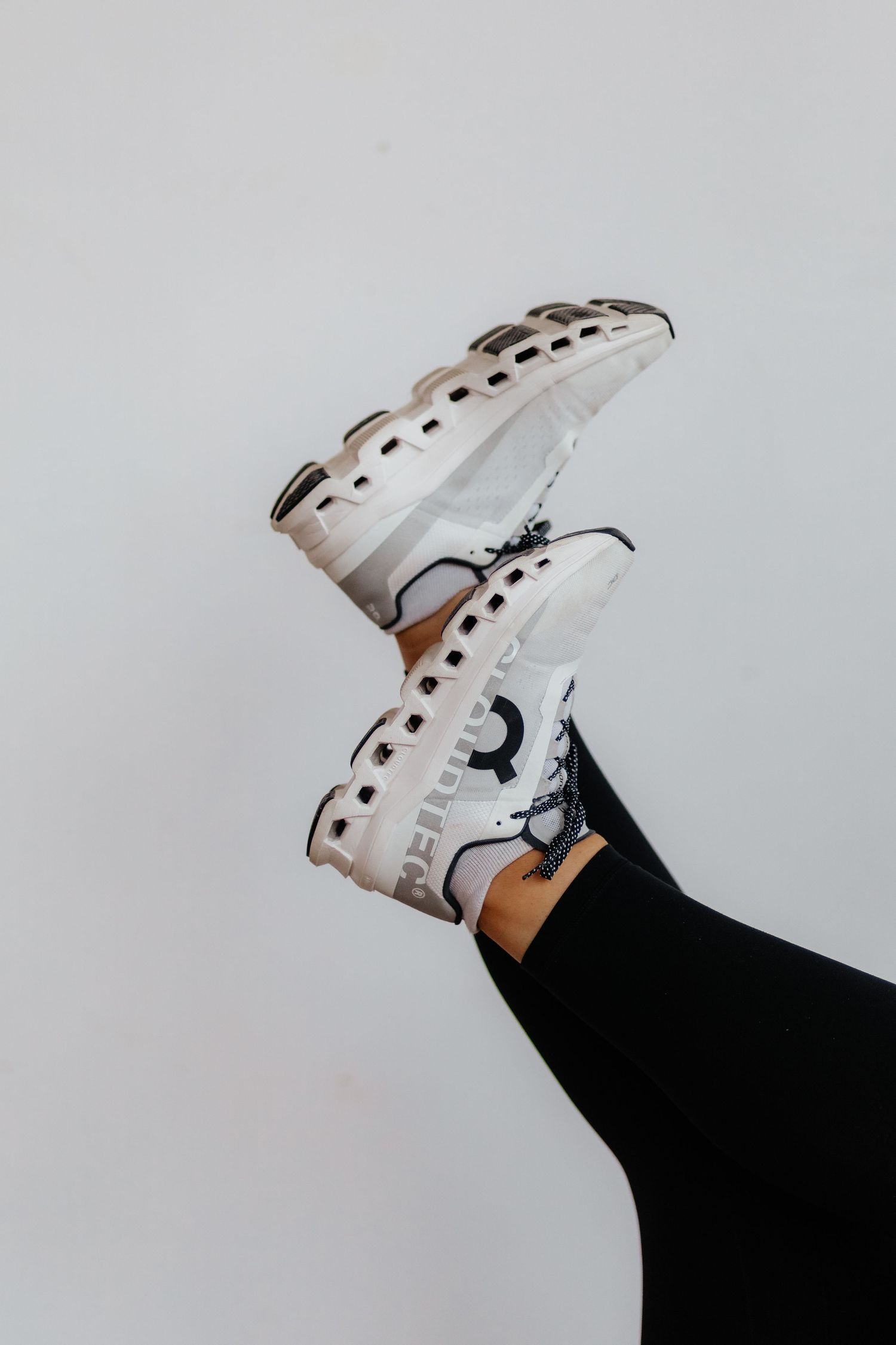 A foot wearing a white leather sneaker with black polka dots and raised against a light gray background.
