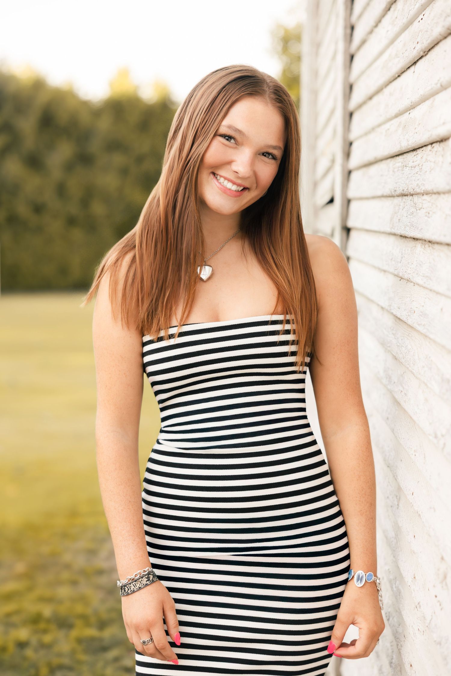 Portrait of someone in a black and white striped dress leaning against a white wall outdoors on a sunny day.