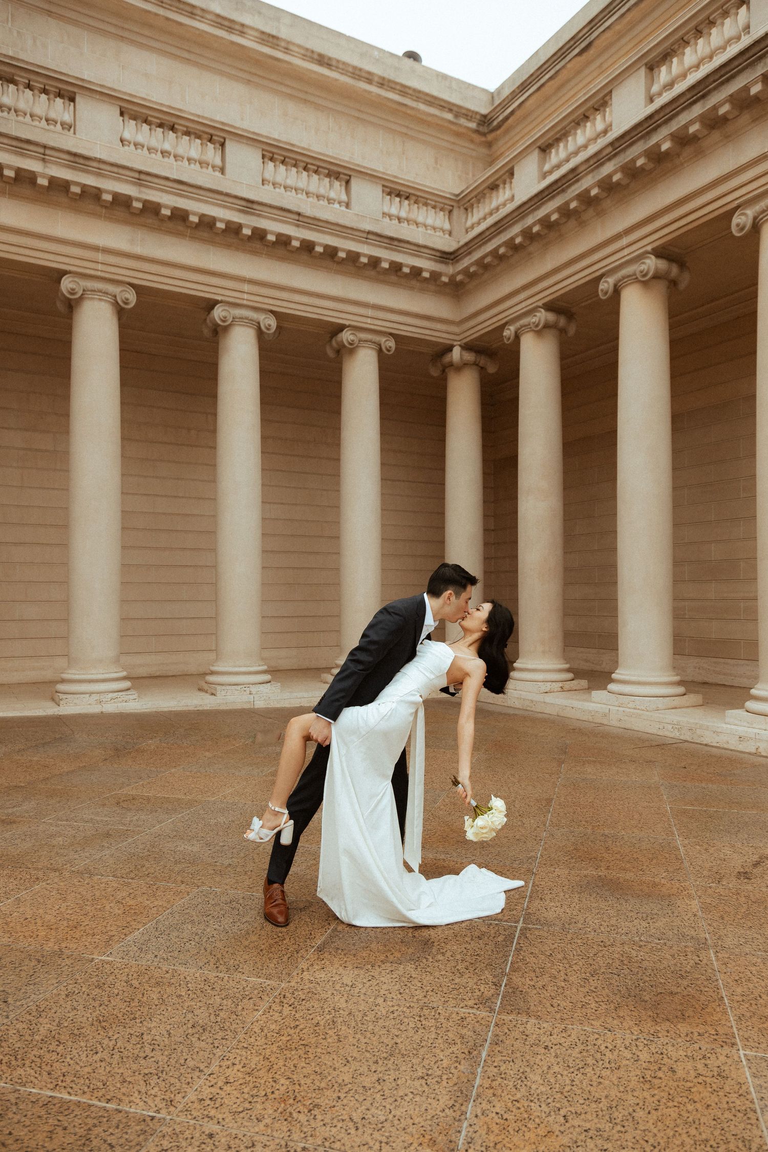 A romantic dip pose between a couple in formal attire inside a classical columned building.