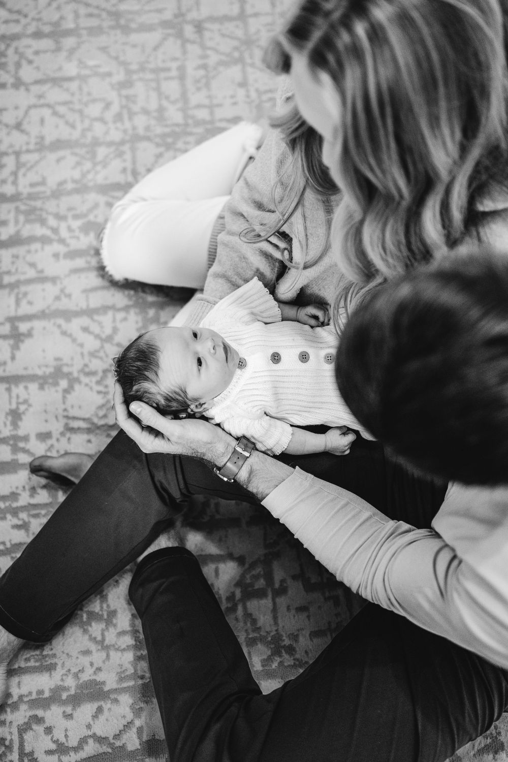 A black and white intimate photo of a baby being held on someone's lap on a patterned carpet.