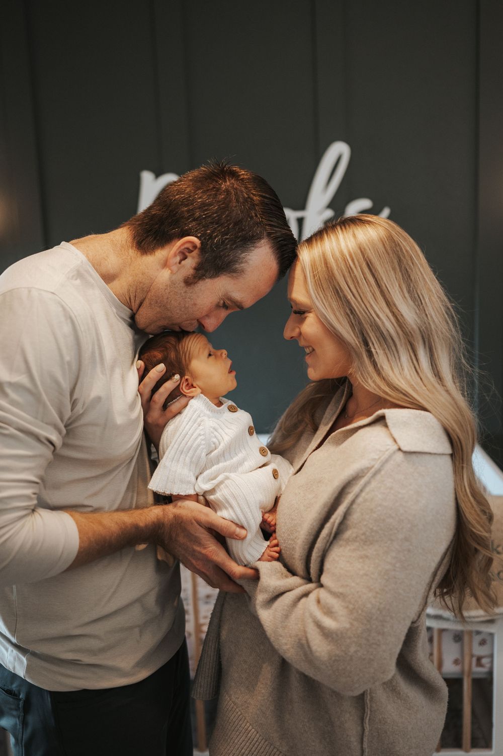 Intimate family moment with couple holding newborn baby in nursery setting.