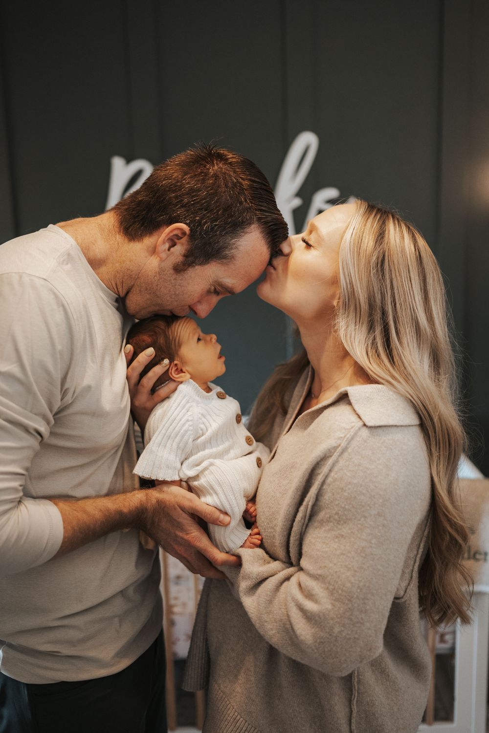 Family shares an intimate moment together with their baby in a warmly lit indoor setting.