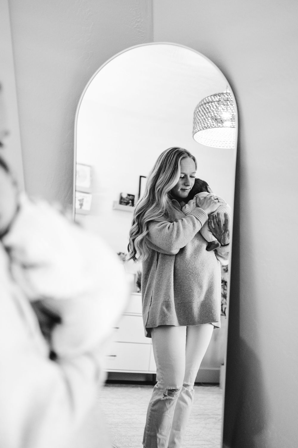 Black and white mirror selfie of someone wearing an oversized sweater and ripped jeans in a bathroom.