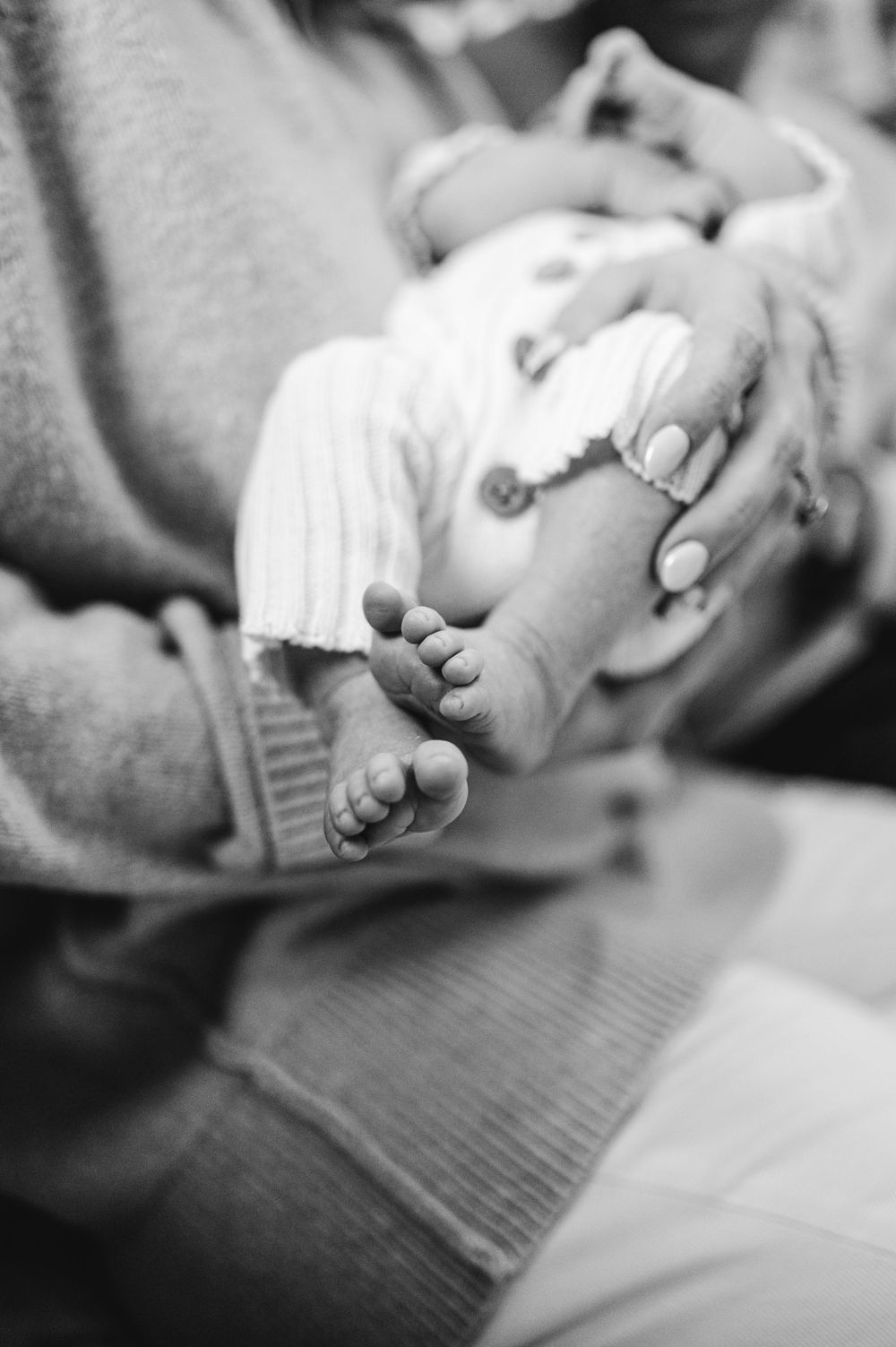 Close-up black and white photograph of tiny newborn baby feet being cradled in gentle hands.