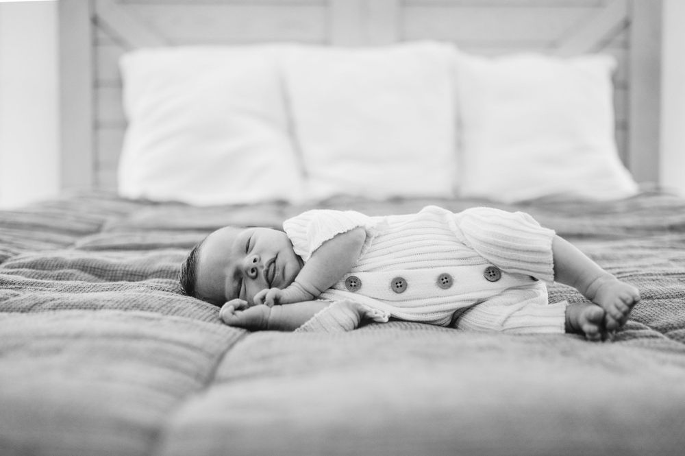 Black and white photo of a sleeping baby wearing polka dot clothing on a bed.