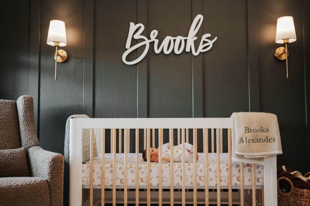 Modern nursery with a white crib, grey accent wall, wall sconces, and custom 'Brooks' name sign above.