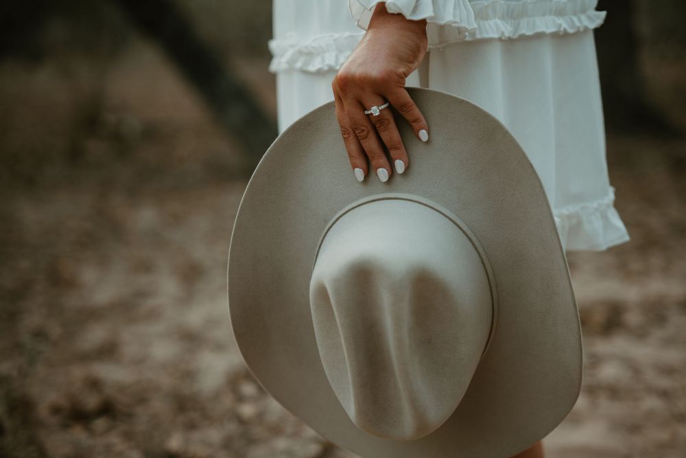 Hand holding a light gray cowboy hat against desert background.