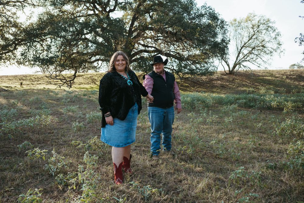 Two people walking together on rustic countryside terrain wearing casual western clothing.